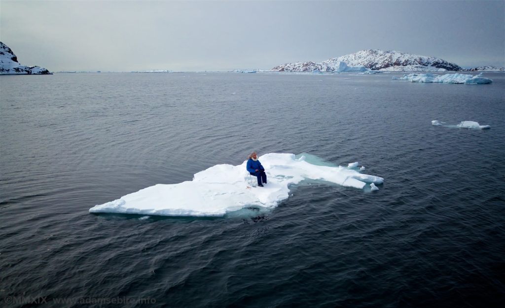 A man sitting on a chair on a small piece of ice in the middle of the sea